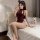 A woman poses on a bed wearing a maroon retro chinese qipao lingerie set, featuring cut-out details and a halter neck design,...