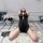 Woman in black retro lace cheongsam lingerie set, kneeling on rug with sheer mesh backless design and vintage-inspired style.