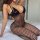 A woman poses on a bed wearing a black sheer fishnet bodysuit with a glossy top, perfect for romantic evening wear.