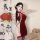 A woman poses elegantly in a red silk velvet qipao, featuring lace-up details and cut-outs. the dress includes a mandarin-sty...