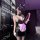 Woman in black bunny lingerie with ears, mask, and apron holding whip in dimly lit room.