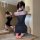 Woman wearing black sheer mesh cheongsam lingerie with cut-out details, posing on massage table in intimate setting.