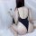 Woman modeling backless black bodysuit swimwear with low-cut design, seated beside dried flowers on white backdrop.