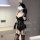 Woman wearing black lace lingerie set with sheer mesh bodysuit, garter stockings, and cat ears in modern room.