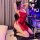 Woman in red lace lingerie set with tie-up details, posing seductively on gaming chair in bedroom setting.