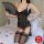 Woman in black lace lingerie set with mesh vest and garter stockings, holding a fan on a bed.