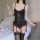 Woman in black lace lingerie set with mesh vest and garter stockings, holding wine glass beside bed with rose petals.