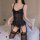 Woman wearing black lace lingerie set with mesh vest, garter straps, and stockings on bed with rose petals.