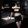 Woman in black seductive lace peek-a-boo two-piece sleepwear set with low-cut bra and matching shorts, posing by sink.
