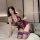 Woman in purple lace lingerie set kneeling on bed, featuring sheer bodice and matching thigh-high stockings.