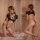 Woman modeling black seductive maid costume lingerie set with cutout details, posing in bedroom setting.