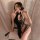 Woman in black lace maid costume sleepwear, sheer and elegant, posing seductively on a chair with soft curtains behind.