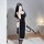 Woman in black seductive nun costume lingerie with lace trim, holding whip, posing for mirror selfie in bedroom.