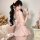 Woman in pink seductive nurse costume with bow back, holding stethoscope, surrounded by teddy bears and soft decor.