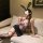 Woman wearing purple floral bodycon skirt set with black lace bunny ears, sheer stockings, and choker on beige sofa.