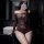 Woman in sheer mesh lingerie set with lace details, posing in bathroom mirror selfie.