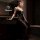 Woman in black seductive no-remove bodysuit with gold floral details, posing in a dimly lit bathroom.