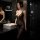 Woman in black sheer bodysuit with floral lace, posing by bathroom sink – seductive no-remove bodysuit set for women.