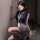 Woman in navy blue sleeveless top and gray skirt with lanyard, posing seductively against a wall.