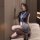 Woman in navy blue sleeveless top and gray pencil skirt, kneeling on beige couch, wearing black heels and white lanyard.