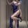 Woman modeling blue lace lingerie set with high slit, sheer straps, and garter details in a modern hallway setting.