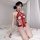 Woman wearing red lace bodysuit with sheer mesh, cut-outs, and ruffled trim on bed with rose petals.