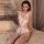 Woman wearing white lace bodysuit with open-crotch design, sitting on bed in elegant bedroom setting.