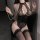 Woman wearing black lace bodysuit with gold chain detailing, sheer mesh panels, and matching thigh-high stockings.