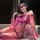 Woman in purple lace lingerie set with sheer mesh robe and stockings, posing seductively on couch.