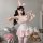 Woman wearing pink sensual lace sheer maid costume with bunny ears, holding teddy bear, posing playfully in cozy room.