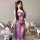 Woman wearing purple sensual lace sleep dress with sheer mesh, high slit, and backless design in cozy bedroom setting.