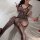 Woman wearing black lace bodysuit and fishnet stockings, posing on white bed with rose petals — sensual lingerie sleep set fo...