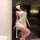 Woman wearing a white, form-fitting sensual lingerie dress with halter neck and side slit, posing in a modern room setting.