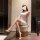 Woman in white sensual lingerie, playful erotic outfit with no-remove naughty costume set, sitting elegantly on ottoman.