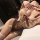 Woman wearing sensual beige and brown lingerie set with ruffles, ribbons, and garter straps, lying on bed in playful pose.