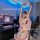 Woman in pink anime-themed open-crotch bodysuit, posing with cat ears and headphones at gaming desk.