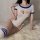Woman wearing white and blue open-crotch bodysuit with matching thigh-high socks, lying on fluffy rug.