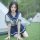 Woman in navy and white sailor-style skirt set kneeling on grass near tents, showcasing the sensual secretarial bodysuit.