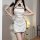 Woman wearing white sheer cheongsam lingerie with black trim, holding a fan in a cozy room setting.