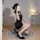 Woman posing in black sheer cheongsam lingerie set with high heels, sitting on circular rug indoors.