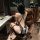 Woman in black bunny girl bodysuit with straps, open-crotch design, sheer fabric, and fishnet stockings, seated on leather ch...