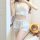 Woman wearing white sheer lingerie sleepwear set with lace trim, featuring a cropped top and shorts, posing beside a plush be...
