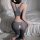 Woman wearing gray ice silk open-crotch yoga pants set with zipper design, kneeling on fluffy rug beside bed.