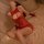 Woman in red lace bodysuit with garter straps and open-crotch design, posing on bed for intimate moments.