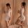 Woman modeling white lace bodysuit with sheer sleeves and tight mini skirt in soft bedroom setting.