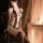 Woman wearing sexy lace bodysuit with rhinestones, sheer lingerie set in warm candlelit room.