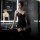 Woman wearing black lace bodysuit with sheer mesh, stockings, and skirt – seductive lingerie set in modern bathroom.