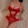 Woman wearing red lace bodysuit with push-up cups and open-crotch design, lying on bed.