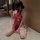 Woman in red lace cheongsam sleepwear set with adjustable ties, sheer design, sitting on floor holding a fan.
