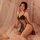 Woman in black lace lingerie sleepwear set with sheer mesh cami and tie-strap nightgown, posing on bed with soft lighting.